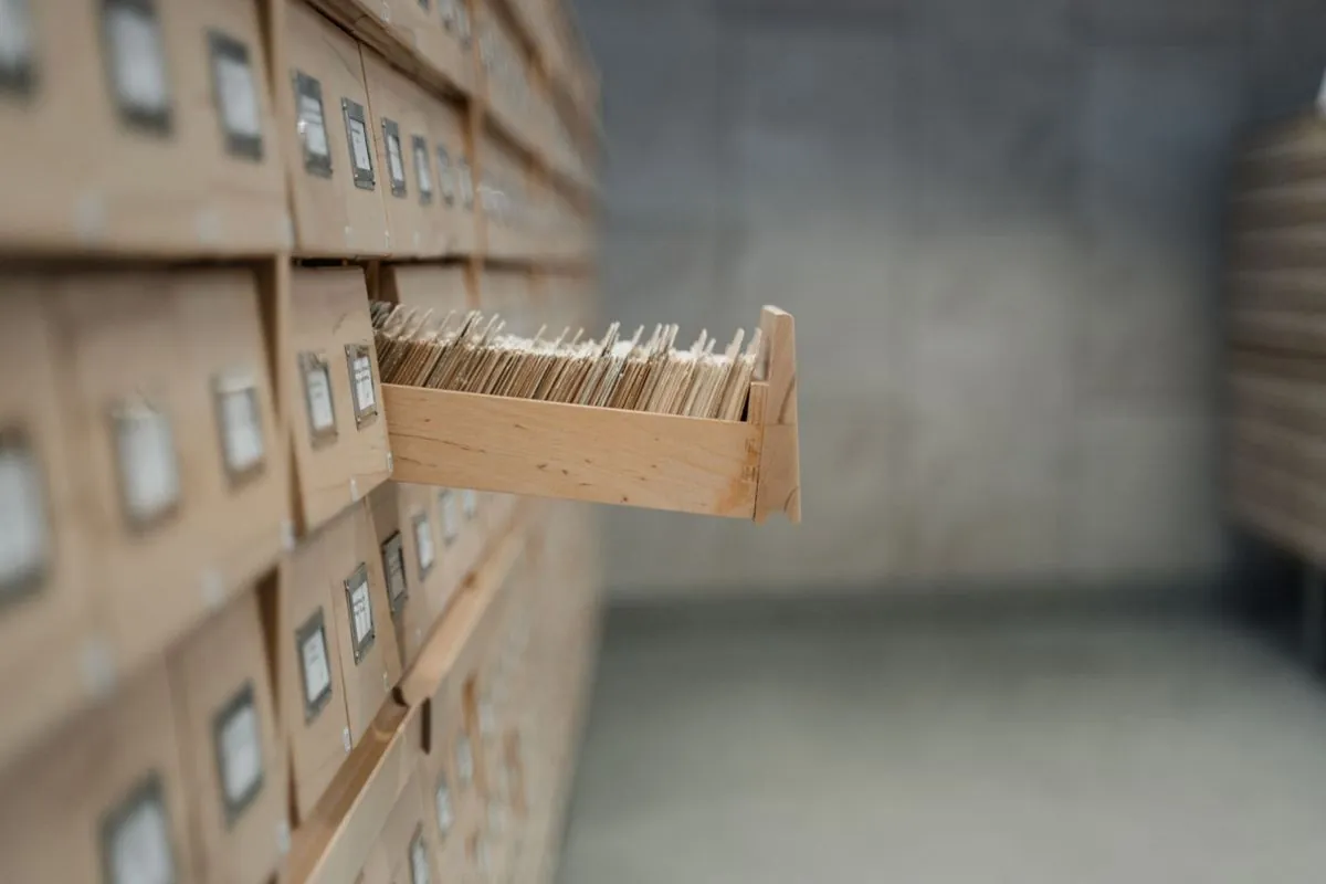 Mani che sfogliano schede di carta dentro il cassetto di uno schedario
