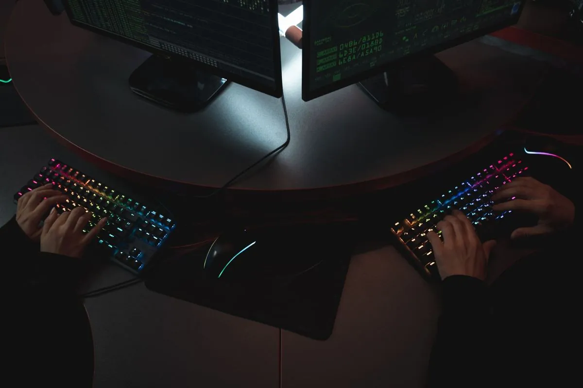 Le mani di chi programma sulla tastiera davanti a un monitor pieno di codice