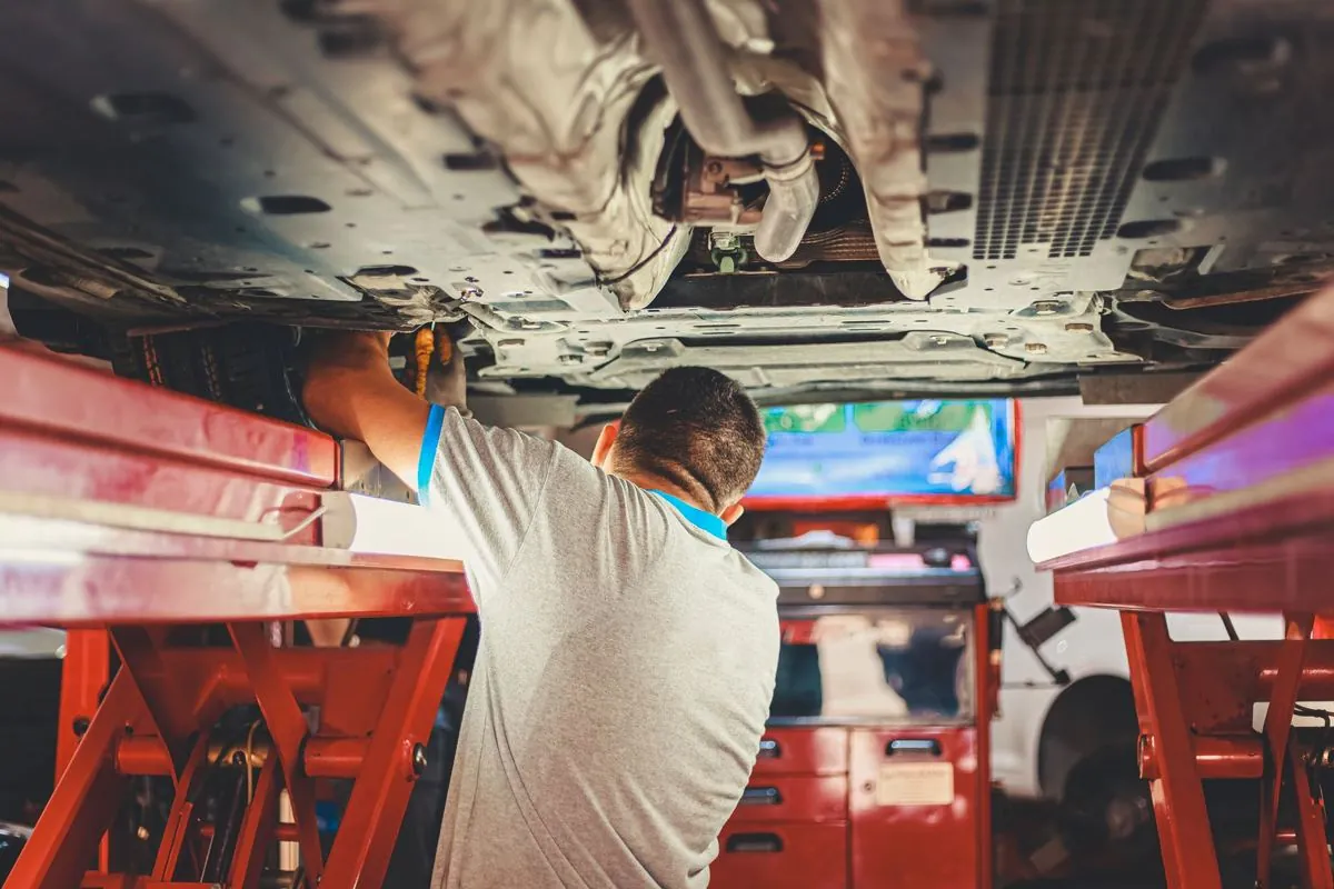 Officina con un’auto sul ponte e un portatile aperto accanto al meccanico